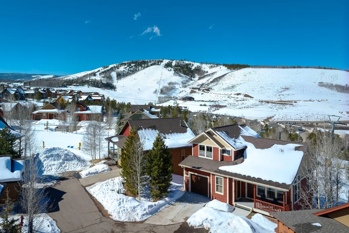 A dramatic exterior panorama capturing snow-covered mountains towering over charming homes under a clear blue sky. The vastness of the landscape invites thoughts of skiing, snowboarding, hiking, and mountain biking, reflecting the range of activities described in the section.