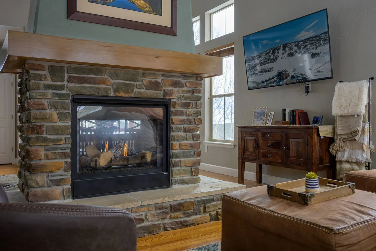 An inviting fireplace scene with a wooden mantel, television, and cozy throws. The ambiance is perfect for gathering to unwind with a warm drink or a movie night after outdoor pursuits.