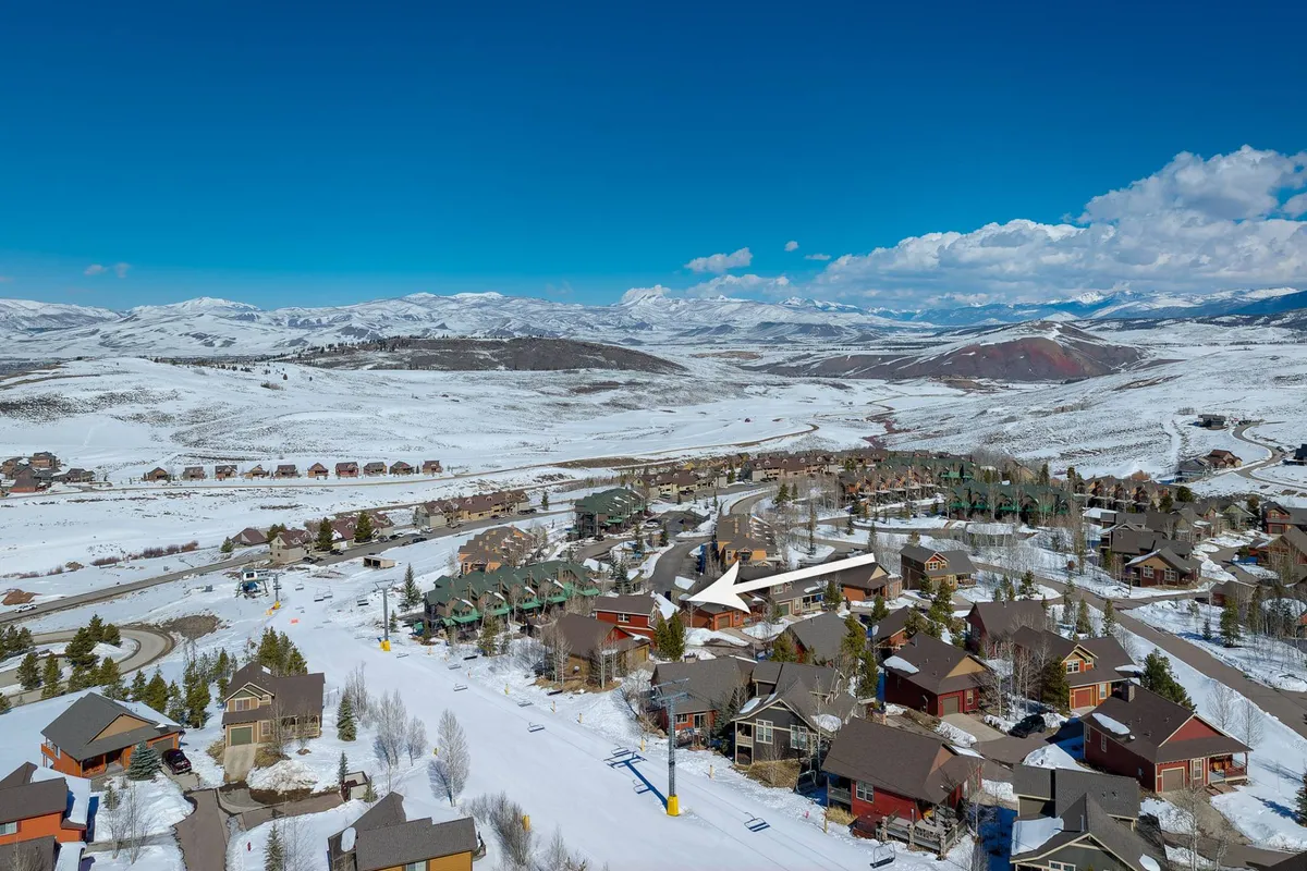 A wide view of the snow-covered landscape, with mountains in the background, residential homes, and a visible ski lift. The setting suggests immediate proximity to outdoor adventures and family-friendly mountain activities.
