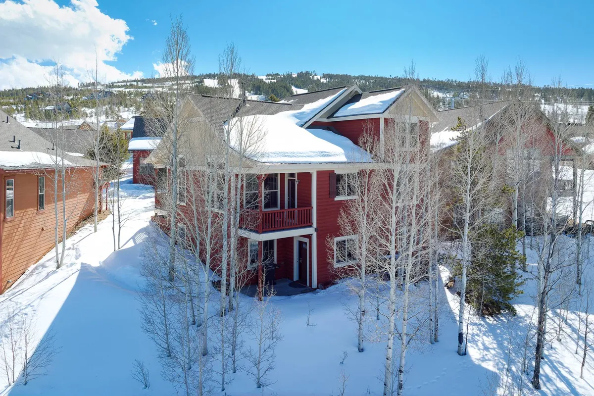 This image showcases the exterior of a cozy red house nestled among snow-covered ground and surrounded by trees. The setting feels tranquil and inviting, offering a clear sense of the home's outdoor environment and immediate access to nature.