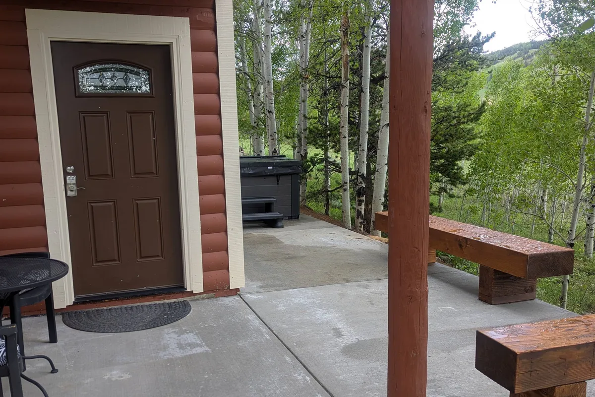 This image shows the front of the house, including a wooden bench and the hot tub, creating a welcoming scene for outdoor relaxation. The mood is cozy, ideal for gathering with friends, watching sunsets, or letting pets lounge under watchful eyes.