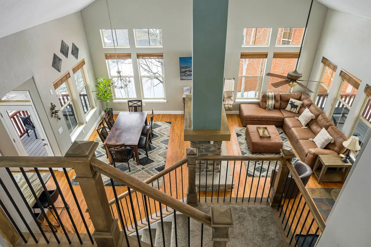 A bright and open area with large windows, a dining table for group gatherings, a plush sectional sofa, and tasteful wall art. Sunlight pours in, offering a seamless blend of comfort and scenic mountain surroundings.