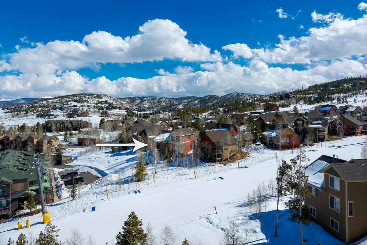 A tranquil wide-angle exterior shot of wooden homes set against a snow-covered landscape, with distant mountains and a clear blue sky in the background. While winter sports are visible, the open trails and expansive setting suggest year-round access to mountain biking and hiking when the snow melts.