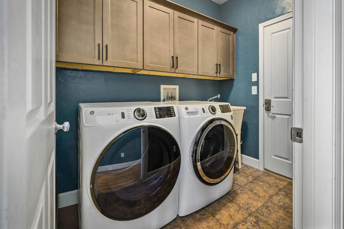 This image shows a laundry area with washer and dryer, cabinets, and a blue accent wall. The space is tidy and organized, offering storage solutions for cleaning supplies and potentially additional outdoor gear. The practical setup reinforces the home's focus on supporting active lifestyles and easy transitions from outdoors to indoors.